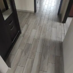 Korytarz wyłożony podłużnymi płytkami imitującymi drewno, widok z góry, ciemna szafka z lustrem po lewej stronie.