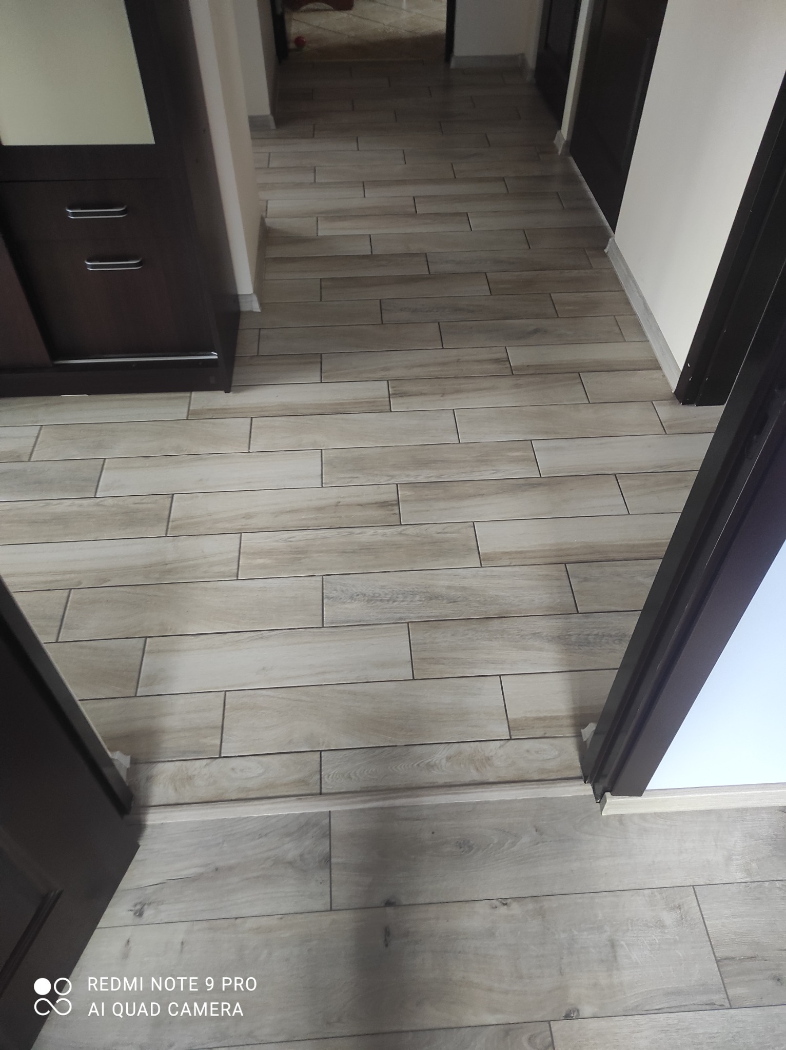 Ułożona podłoga z płytek imitujących drewno w korytarzu, widok z góry, ciemne futryny drzwi.