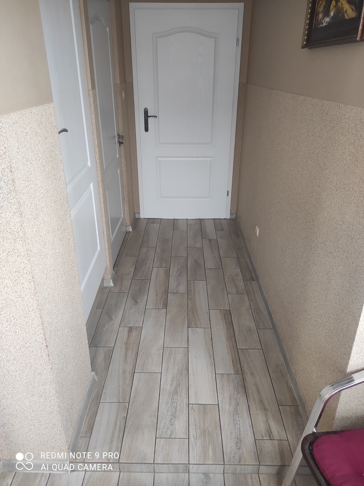 Korytarz z nową, drewnopodobną podłogą z płytek, ściany z fakturą baranka, widoczne dwie białe, klasyczne drzwi.