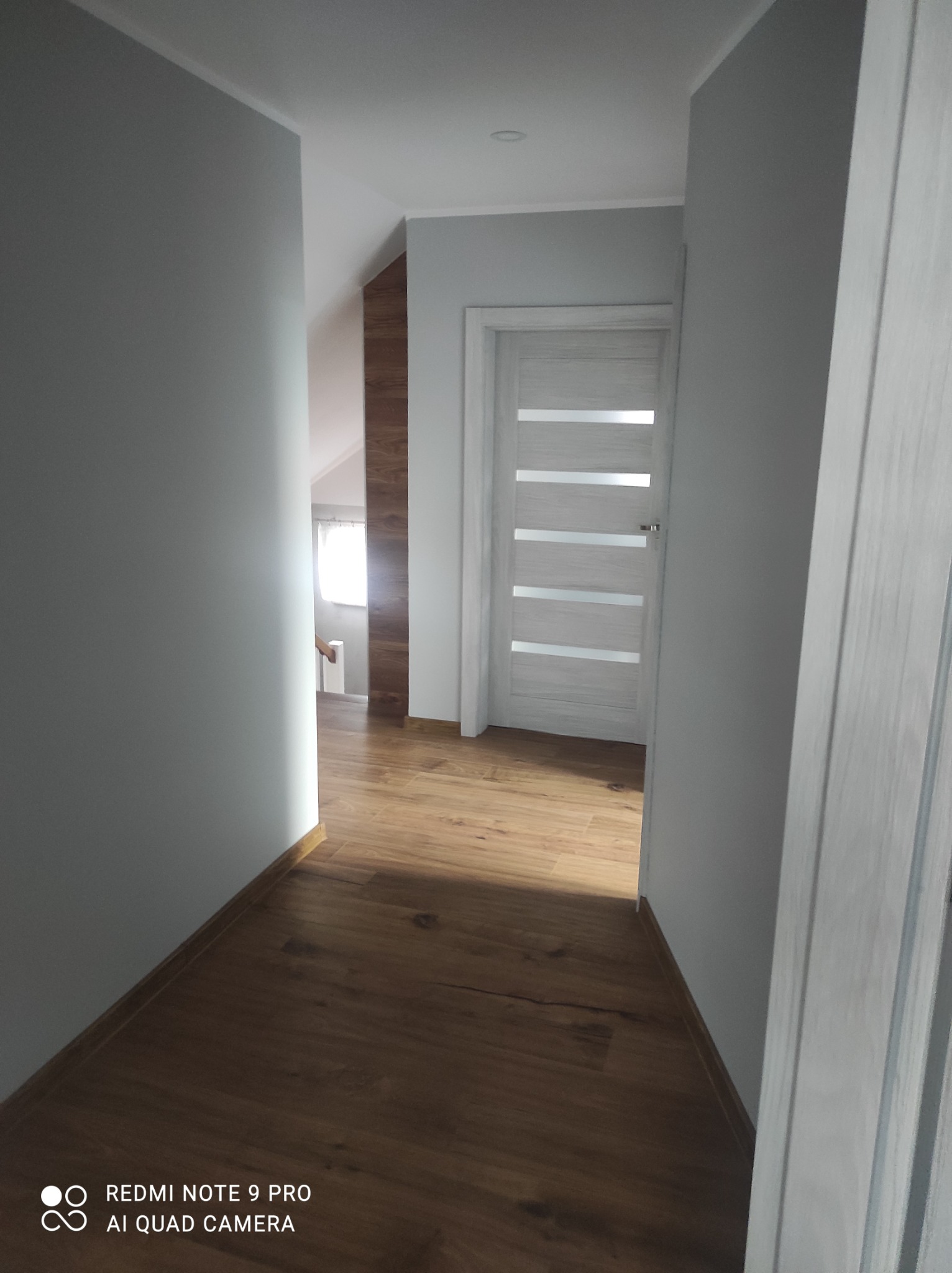 Wnętrze korytarza z drewnianą podłogą, szarymi ścianami i białymi drzwiami z poziomymi przeszkleniami, widok z perspektywy podłogi.