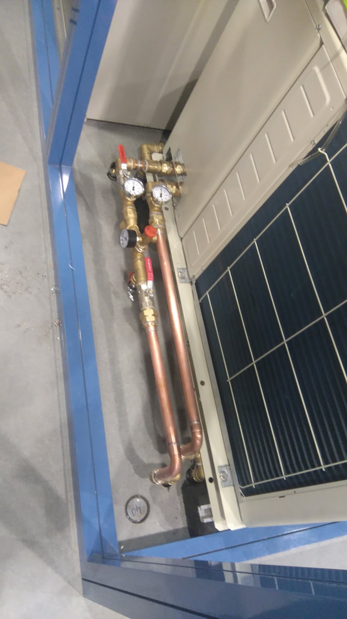 Podłączenie miedzianych rur z manometrami do jednostki klimatyzacyjnej, widoczne elementy instalacji i chłodnica.