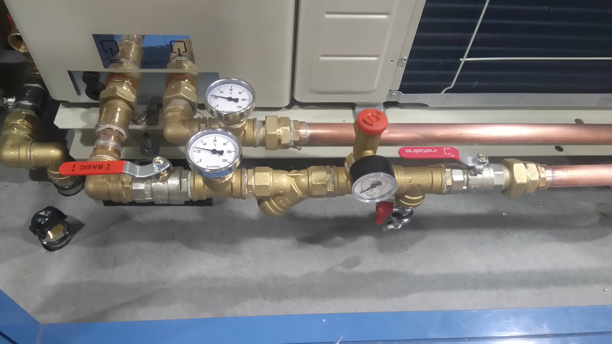 Zestaw rur miedzianych i zaworów z manometrami podłączonych do urządzenia klimatyzacyjnego, widoczne elementy instalacji z bliska.