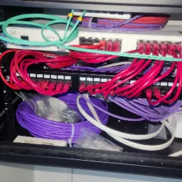Szafa rack z zainstalowanym switchem Cisco, panelem krosowym CAT.6 i okablowaniem w kolorach: czerwonym, fioletowym, białym i zielonym. Widoczne oznaczenia portów na panelu krosowym.