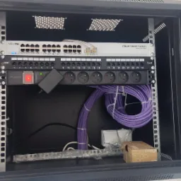 Szafa rack z zamontowanym switchem Mikrotik Cloud Smart Switch, panelem krosowniczym Cat.6, listwą zasilającą Pulsar oraz uporządkowanymi kablami sieciowymi w kolorze fioletowym.