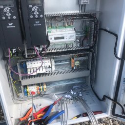 Wszystko w czasie - Otwarta szafa sterownicza z dwoma falownikami Danfoss VLT Micro Drive, widoczne kable, bezpieczniki i narzędzia elektryczne. Elementy sterowania wewnątrz obudowy.