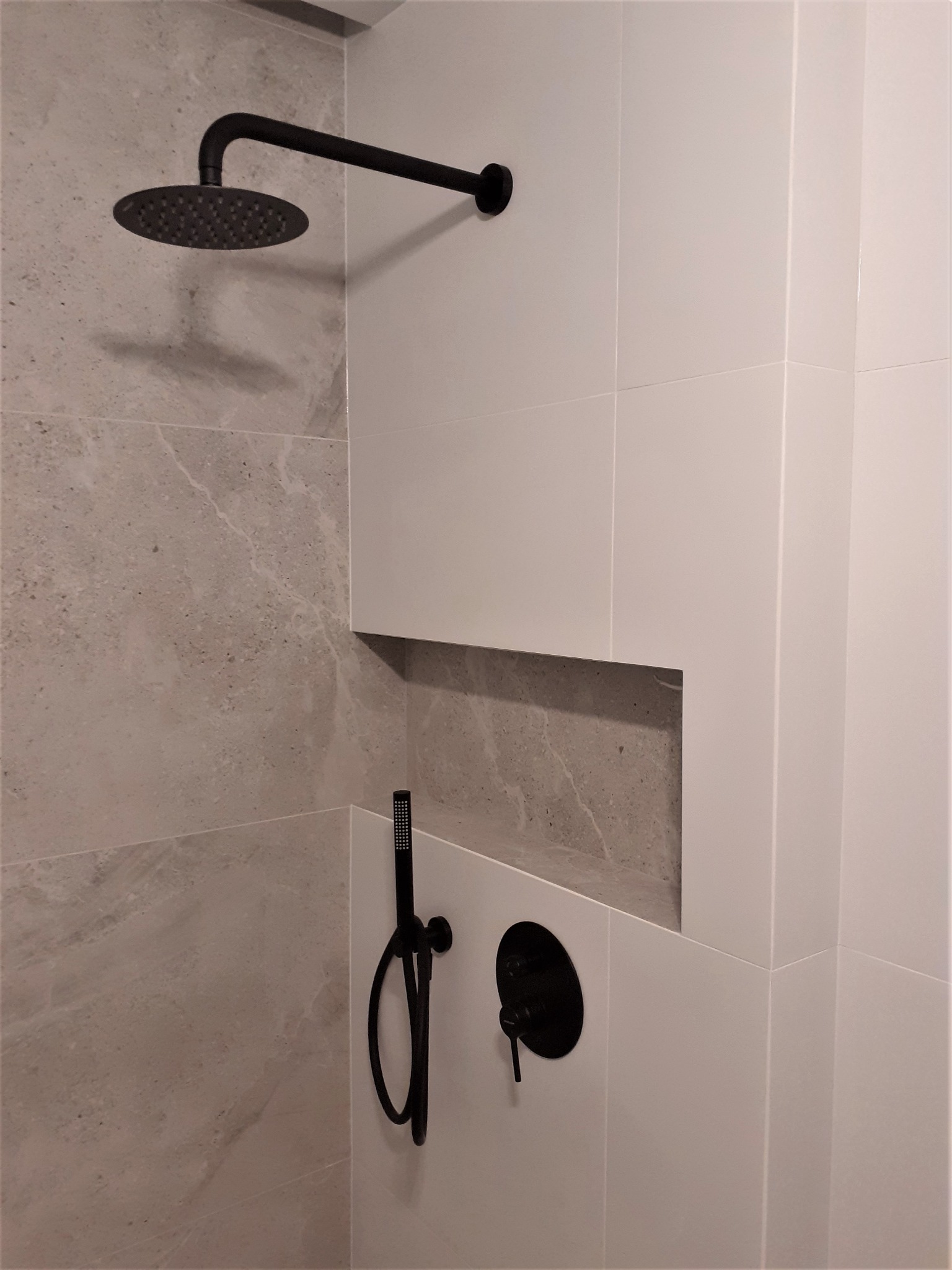 Nowoczesna kabina prysznicowa z deszczownicą i baterią w kolorze czarnym, wykończona płytkami w odcieniach szarości i bieli, z wnęką w ścianie.