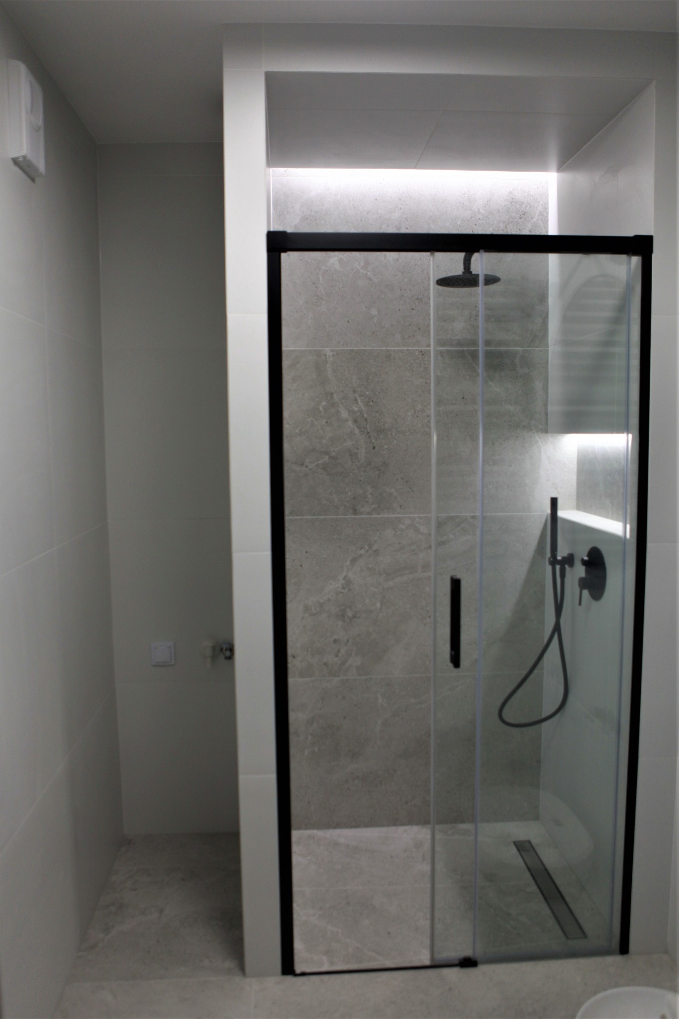 Nowoczesna kabina prysznicowa z czarnymi profilami i deszczownicą, szare płytki imitujące kamień, podświetlenie LED w górnej części kabiny.