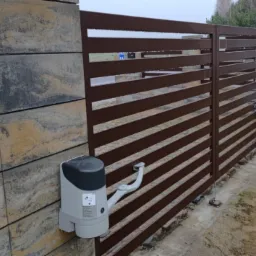 Nowoczesna brama wjazdowa z poziomymi przęsłami w kolorze brązowym, zamontowana na słupkach z dekoracyjnych bloczków betonowych, wyposażona w automatykę z szarą obudową napędu.