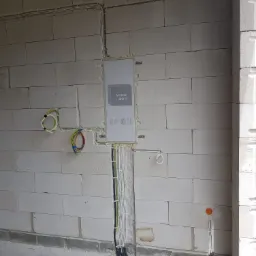 Rozdzielnica elektryczna podtynkowa w surowym stanie, widoczne przewody w ścianie z betonu komórkowego, czarne rury karbowane przy podłodze.