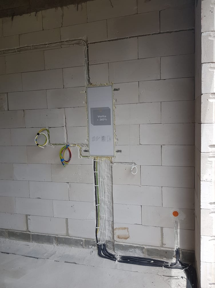 Rozdzielnica elektryczna podtynkowa w surowym stanie, widoczne przewody w ścianie z betonu komórkowego, czarne rury karbowane przy podłodze.