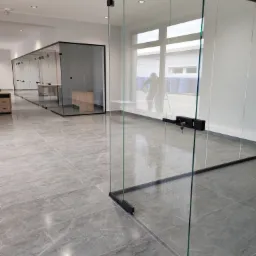 Biuro z przeszklonymi ścianami działowymi; na dalszym planie osoba na drabinie, prawdopodobnie wykonująca prace porządkowe.