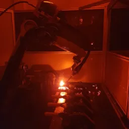 Zautomatyzowane stanowisko spawalnicze z robotem KUKA w trakcie pracy, widoczne iskry i intensywne pomarańczowe światło procesu.