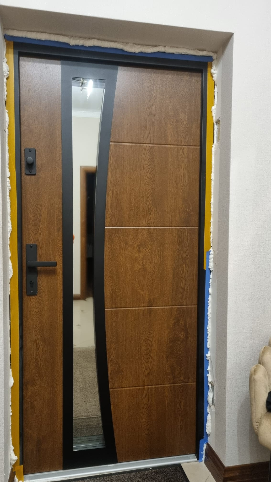 Nowoczesne drzwi z przeszkleniem i drewnopodobnym wykończeniem, osadzone w ościeżnicy z widoczną pianką montażową, sugerujące świeży montaż.