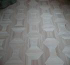 Ułożona jasna podłoga z płytek w kształcie klepsydry, tworząca wzór na całej powierzchni. Widok z góry, lekki kąt, oświetlenie naturalne.