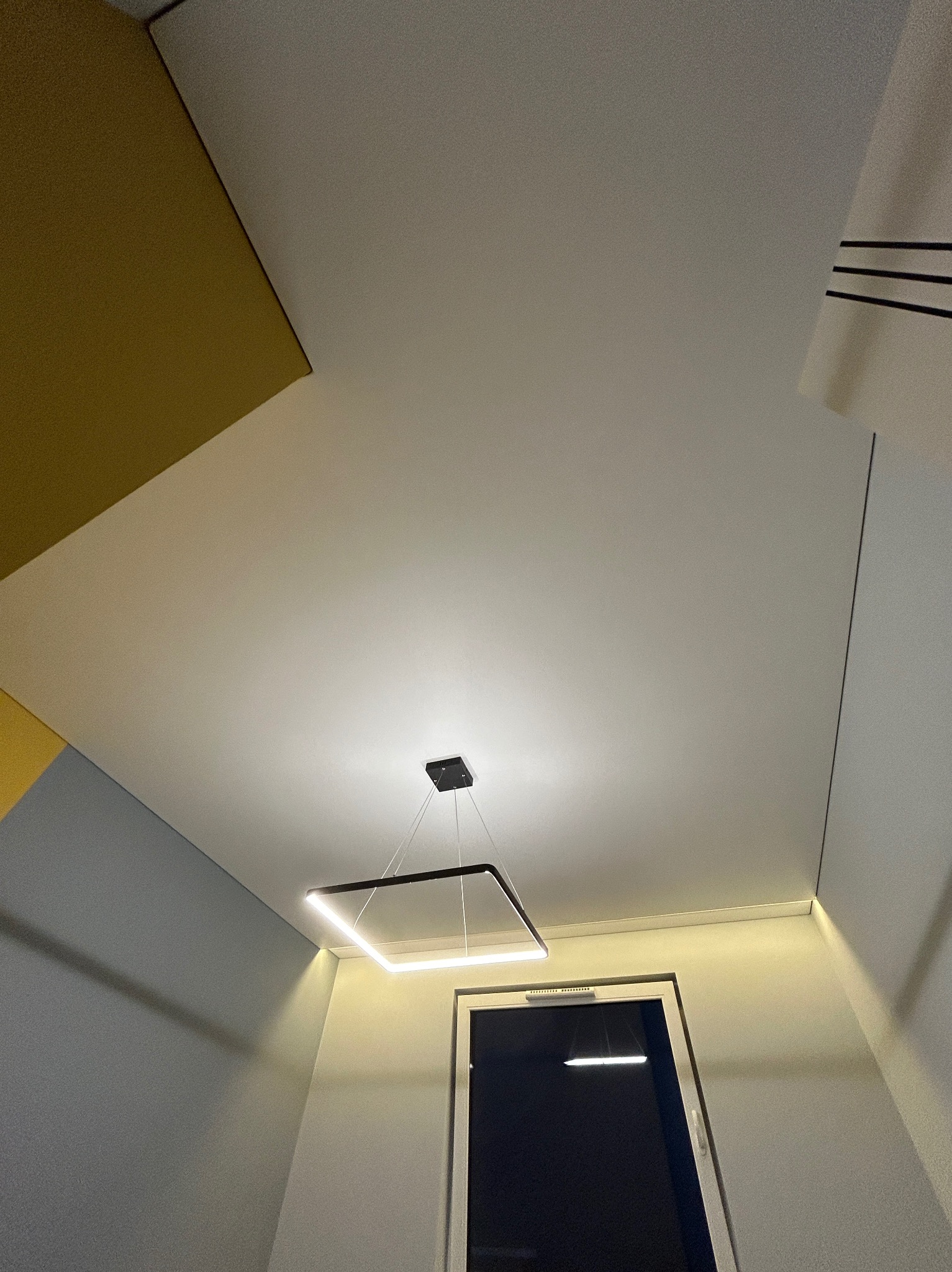 Nowoczesny, biały sufit z podwieszanym oświetleniem LED w kształcie kwadratu i widocznym oknem w tle.