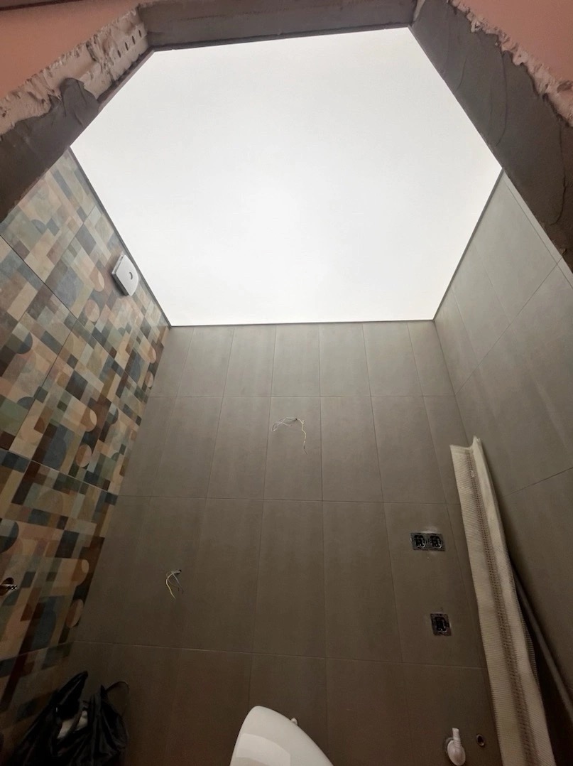 Widok z dołu na heksagonalny, biały sufit w łazience z częściowo wykończonymi ścianami i widocznymi przewodami elektrycznymi.