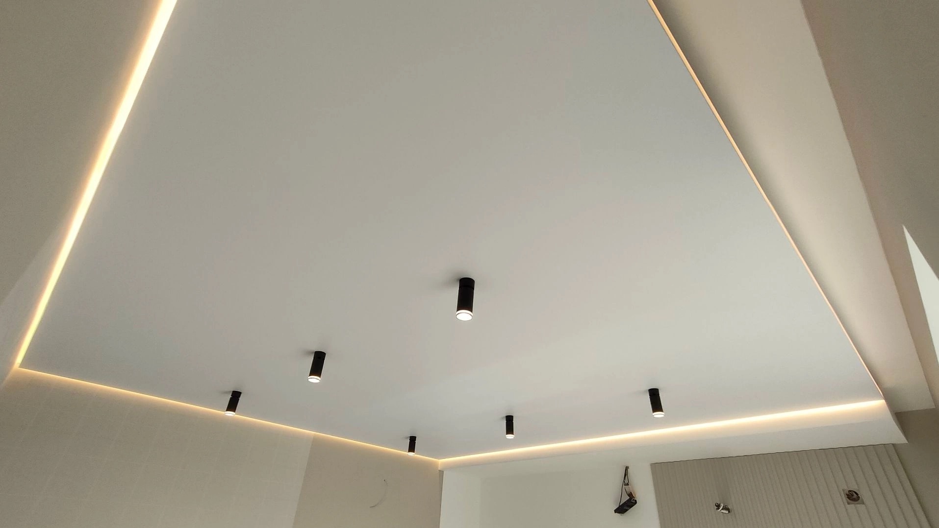 Biały sufit napinany z oświetleniem LED po obwodzie i sześcioma punktowymi lampami w czarnych obudowach.
