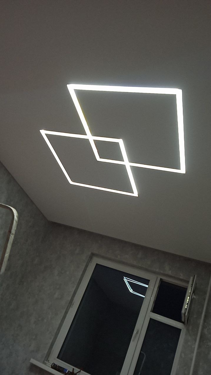 Nowoczesny sufit z podświetleniem LED w kształcie dwóch przecinających się kwadratów, widok z dołu, okno z otwartym skrzydłem w tle.