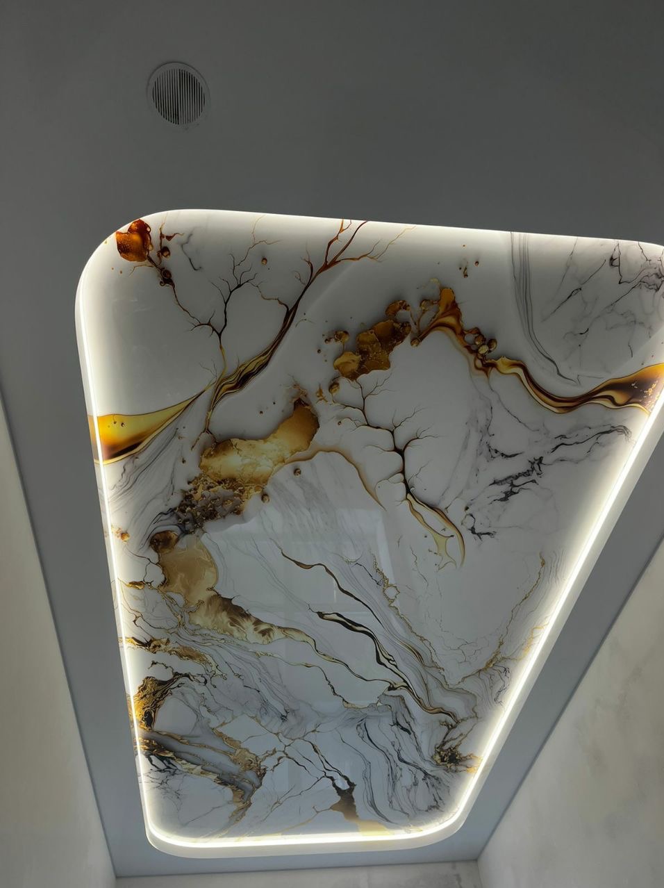 Nowoczesny, podświetlany sufit o trójkątnym kształcie z motywem marmuru w odcieniach bieli, złota i czerni, widziany z dołu.