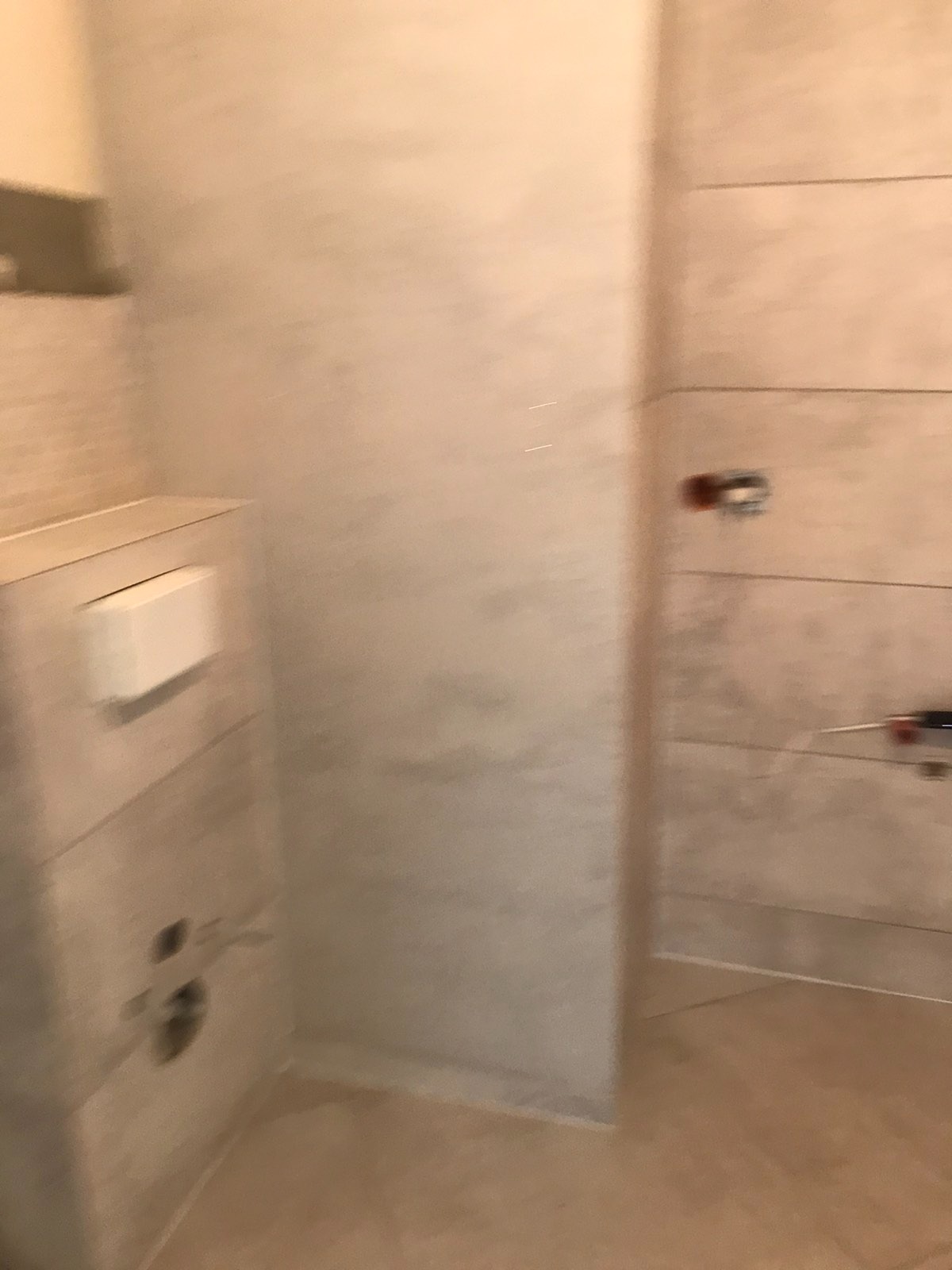 Niedokończona łazienka z beżowymi płytkami, widoczny stelaż podtynkowy WC i wystające kable elektryczne.