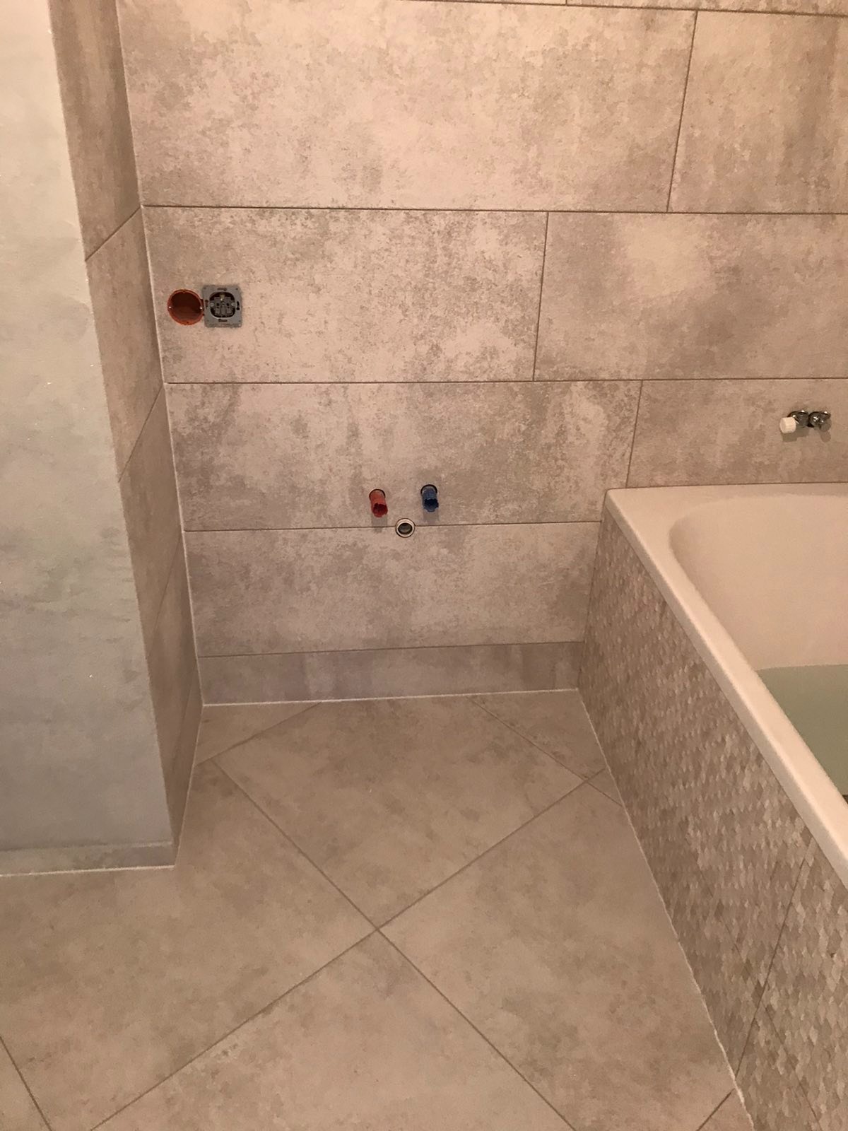 Wykończona łazienka z beżowymi, poziomymi płytkami ściennymi o teksturze kamienia, dopasowanymi płytkami podłogowymi ułożonymi w karo oraz wanną z mozaikową obudową.