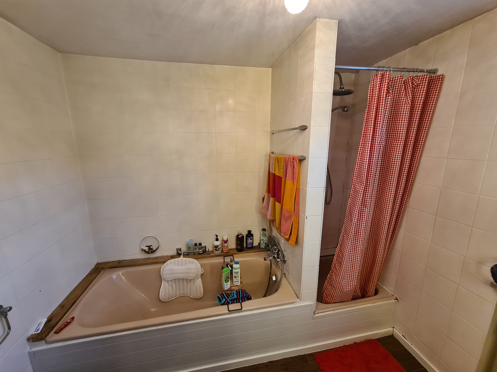 Łazienka z wanną w odcieniach beżu i czerwieni, wyposażona w prysznic z czerwoną zasłoną w kratę, ręczniki i liczne kosmetyki.