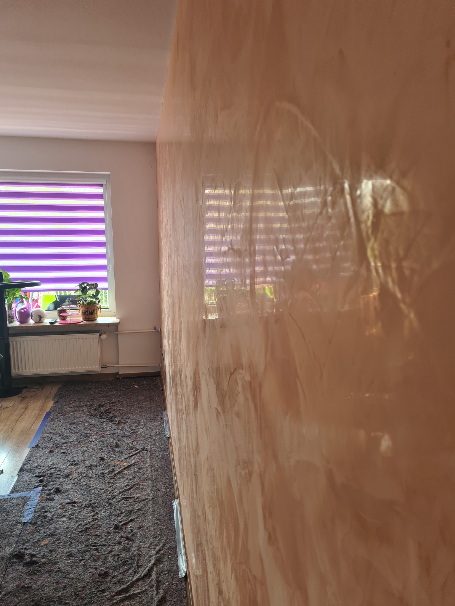 Ściana z efektem dekoracyjnym w odcieniach brązu i beżu, zabezpieczona podłoga z widocznym oknem z żaluzjami w tle.