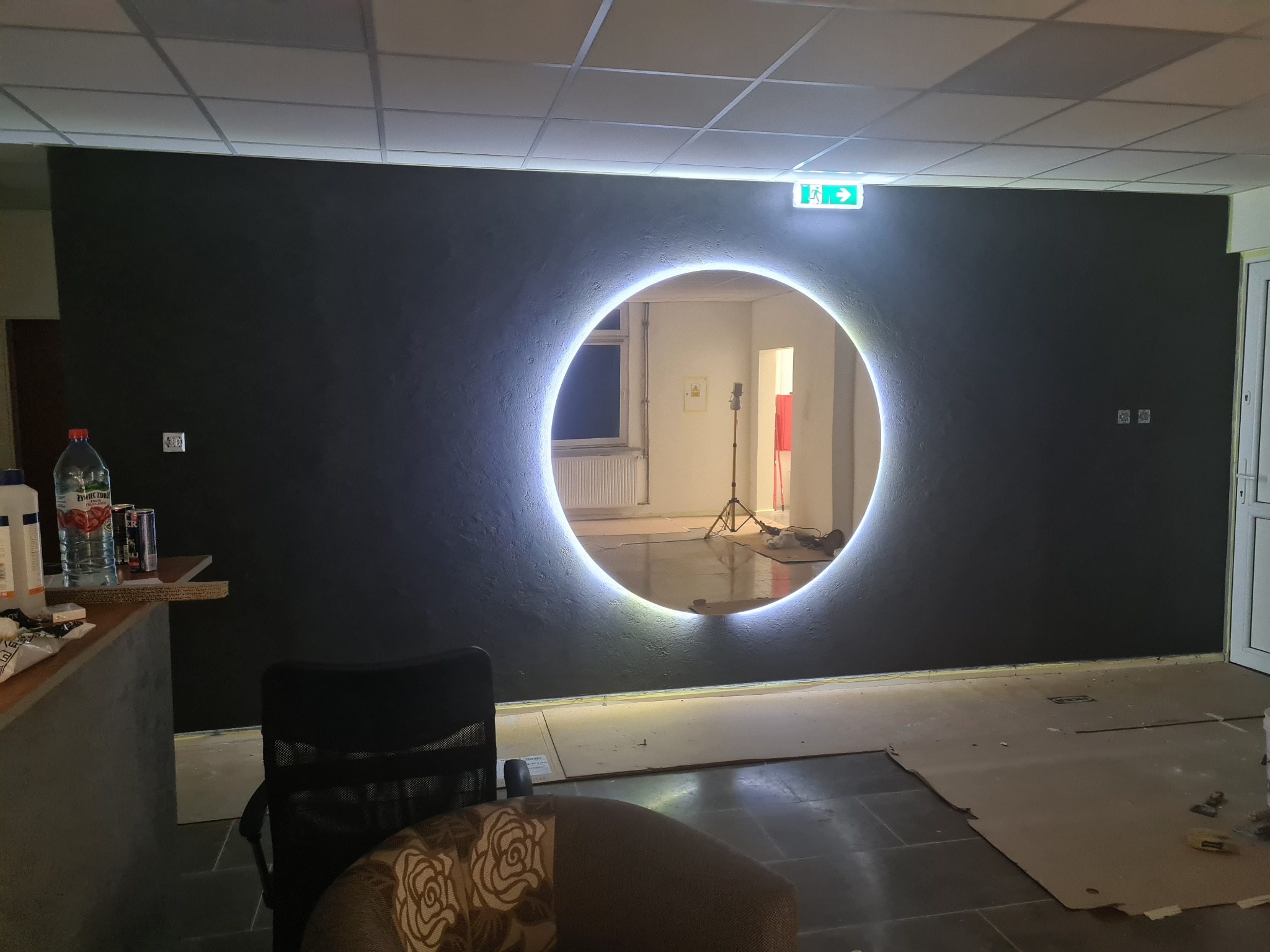 Czarna ściana z dekoracyjnym, okrągłym oświetleniem LED, tworzącym iluzję portalu; widoczne niedokończone prace wykończeniowe na podłodze i elementy wnętrza w tle.