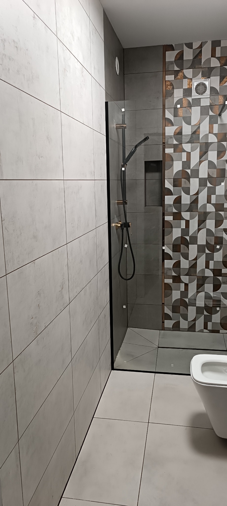 Nowoczesna łazienka z kabiną prysznicową typu walk-in, wykończona płytkami w odcieniach szarości i bieli, z akcentem dekoracyjnej mozaiki na ścianie.