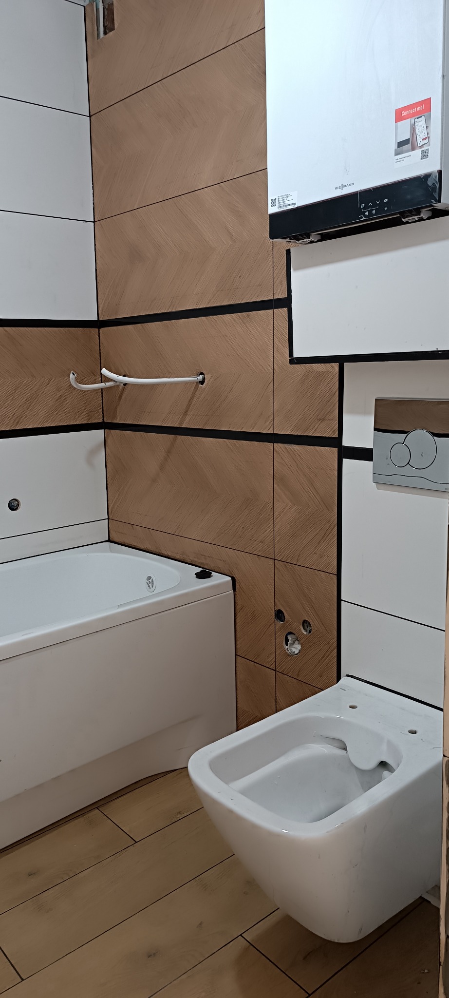 Nowoczesna łazienka: biała wanna i bidet, płytki w odcieniach brązu i bieli z czarnymi akcentami. Na ścianie piec gazowy Viessmann.