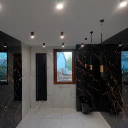 Elegancka łazienka z marmurowymi płytkami, czarnym grzejnikiem i wiszącą toaletą. Nowoczesne oświetlenie punktowe i designerskie lampy wiszące.