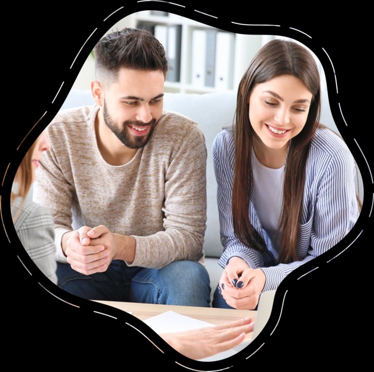 Spotkanie zespołu projektowego: uśmiechnięty mężczyzna w swetrze i kobieta w bluzce w paski analizują dokument, na stole widoczne dłonie trzeciej osoby, w tle regał z segregatorami.