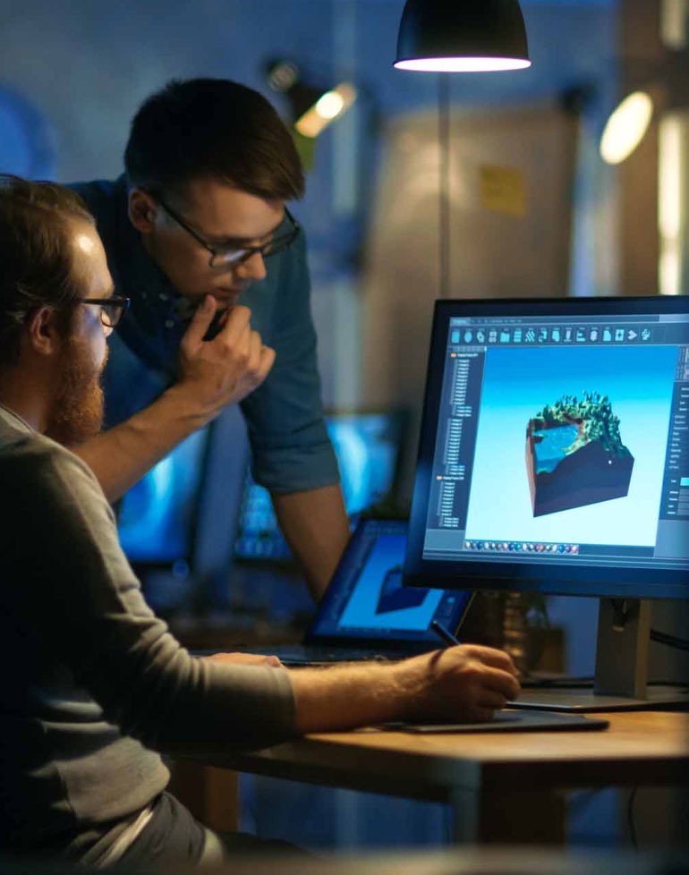 Dwóch mężczyzn w okularach pracuje nad projektem 3D krajobrazu na monitorze komputera z użyciem tabletu graficznego, w tle widoczny drugi monitor.