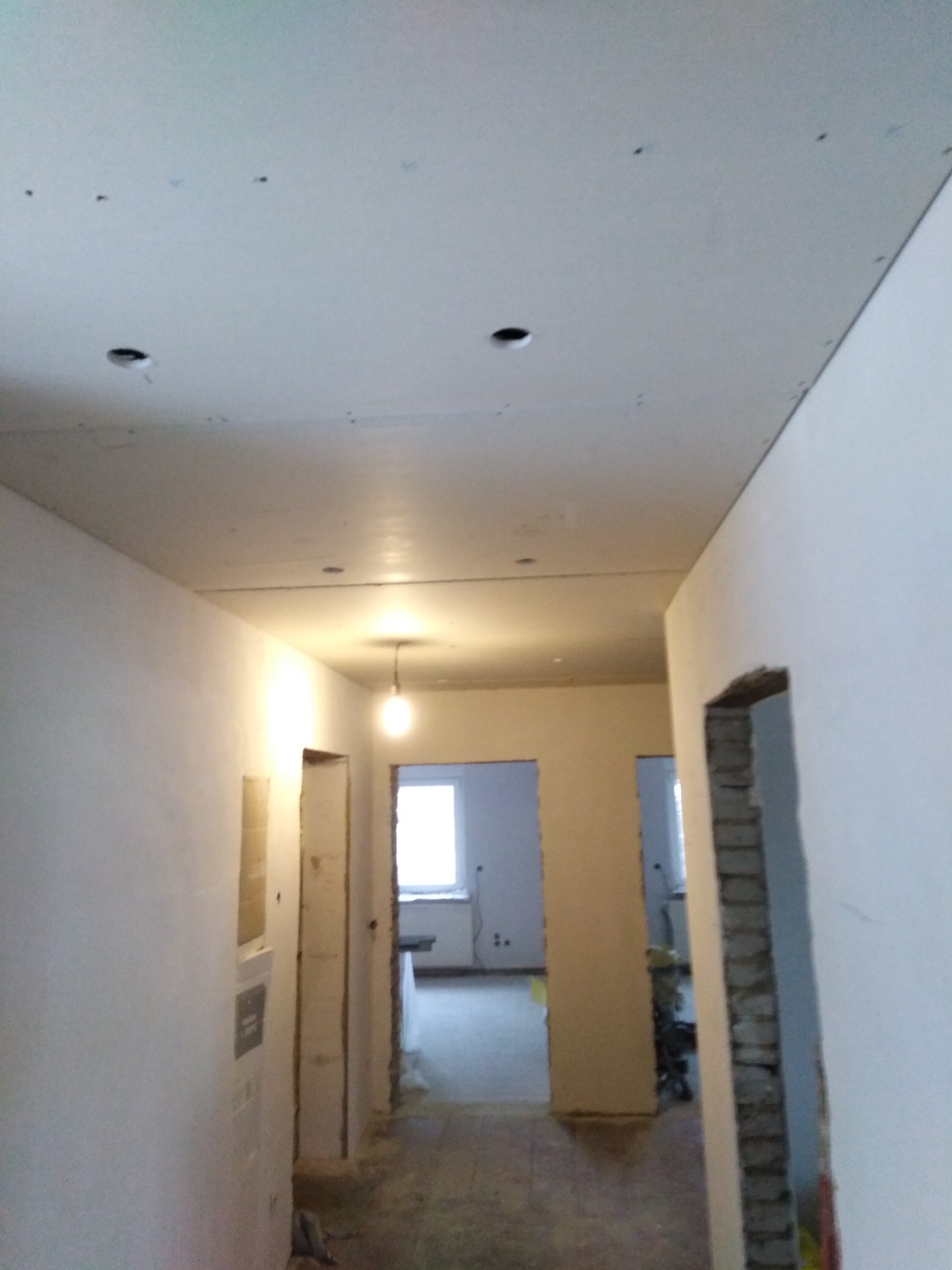 Wnętrze w trakcie montażu płyt karton gips na suficie, widoczne otwory na oświetlenie i surowe ściany w jasnym odcieniu.