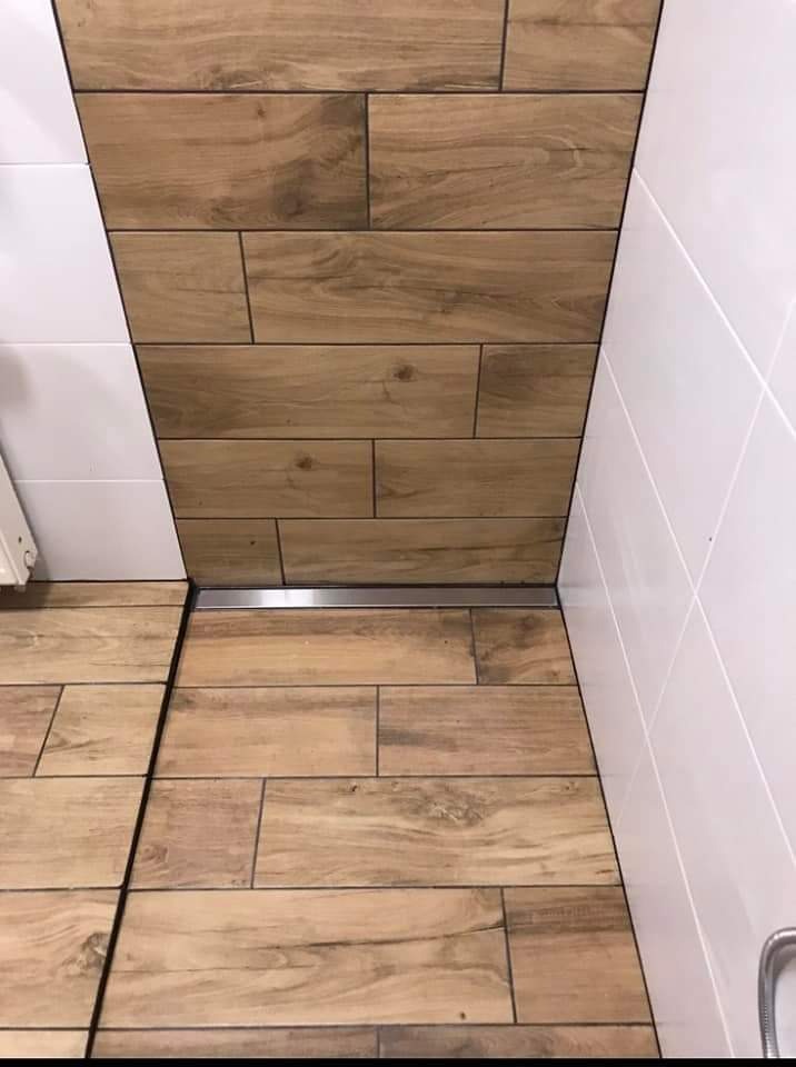 Wykończona podłoga w łazience z płytek imitujących drewno, z odpływem liniowym i białymi płytkami ściennymi.