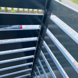 F-tech - Nowoczesna, czarna balustrada balkonowa z poziomych profili, widok z góry, w tle zieleń i fragment ulicy.