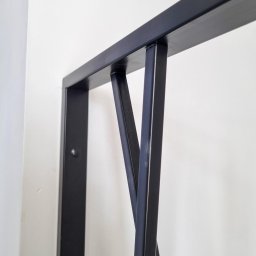 F-tech - Fragment czarnej, metalowej konstrukcji przymocowanej do ściany, z ukośnymi elementami tworzącymi geometryczny wzór.