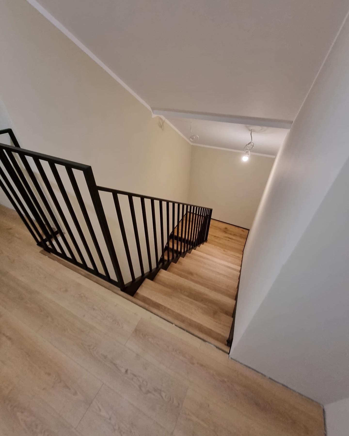 Nowoczesne schody z drewnianymi stopniami i czarną, minimalistyczną balustradą, widok z góry, oświetlenie punktowe.