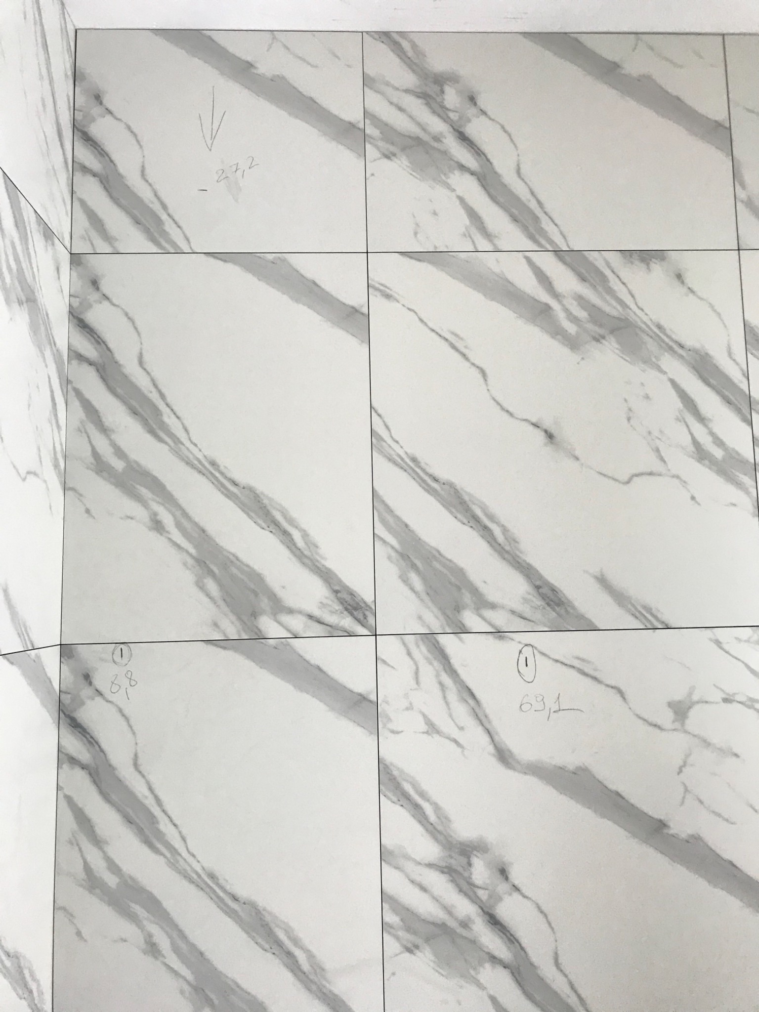 Białe płytki imitujące marmur ułożone na podłodze i ścianie, z naniesionymi ołówkiem wymiarami i oznaczeniami.