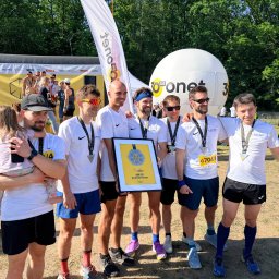 GetThatSpeed - Gabriel Mikołajewski - Drużyna w białych koszulkach z medalami i dyplomem za 3. miejsce w maratonie sztafet firmowych Tetra Pak, na tle sceny i balonu Onet.