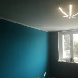 Pomieszczenie po malowaniu: ściana w kolorze turkusowym z białym sufitem i listwą, widoczne okno z narzędziami i butelkami na parapecie, nowoczesna lampa sufitowa.