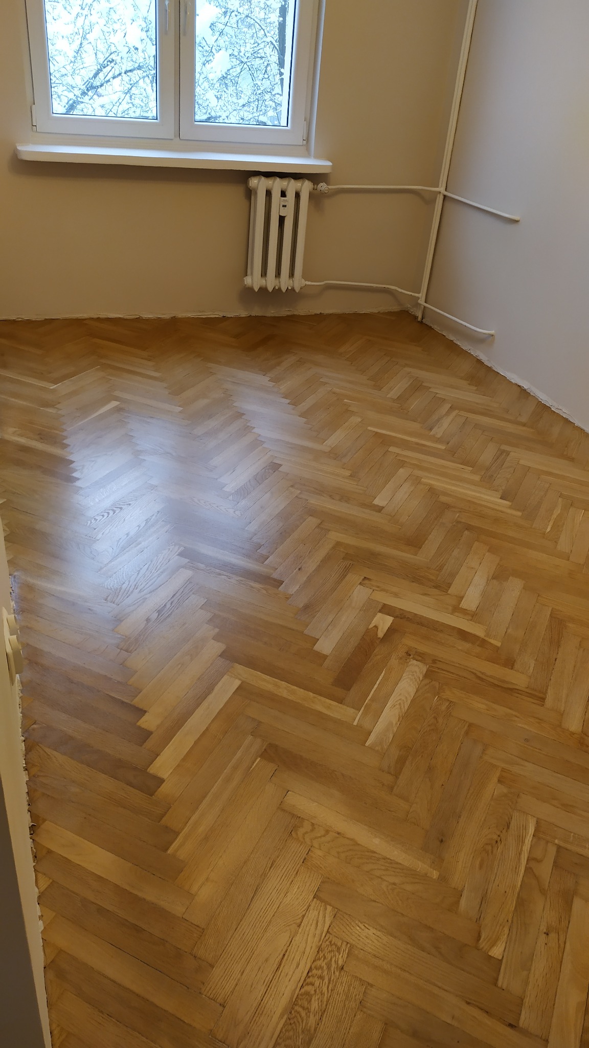 Ukończona podłoga z parkietu ułożonego w jodełkę w Białymstoku, widok na grzejnik i okno z widokiem na ośnieżone drzewa.