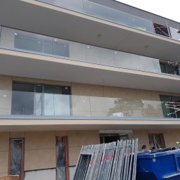 Jakub Polcyn - Wielopiętrowy budynek w trakcie wykańczania elewacji, z widocznymi rusztowaniami, kontenerem na odpady i zabezpieczonymi folią oknami i drzwiami na parterze.