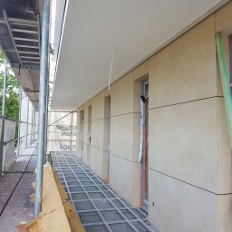 Jakub Polcyn - Elewacja budynku w trakcie montażu paneli elewacyjnych, widoczne rusztowanie i profile montażowe.