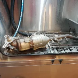 Filtr cząstek stałych DPF wewnątrz metalowej komory czyszczącej, widoczne przewody i dysze