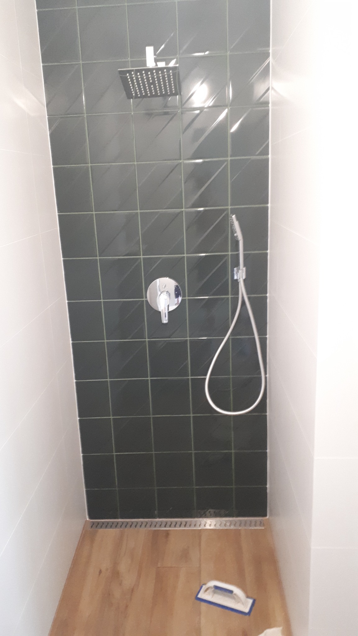 Wykończona kabina prysznicowa z ciemnozielonymi płytkami i deszczownicą w Gryfinie, z widocznym odpływem liniowym i narzędziem do fugowania.