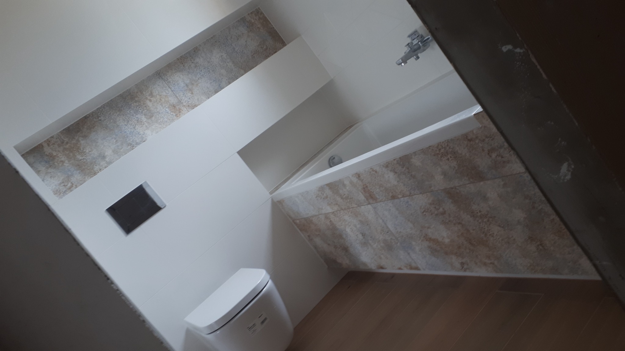 Wykończona łazienka z płytkami imitującymi kamień na ścianach i obudowie wanny, wisząca toaleta z ukrytym spłukiwaniem, oraz drewnopodobna podłoga.