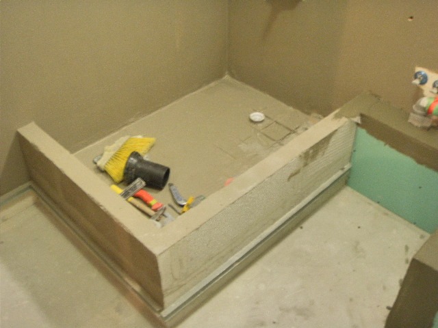 Przygotowanie brodzika prysznicowego: widoczne narzędzia, szczotka, poziomica, oraz zabudowa z płyt w kolorze beżowym i zielonym.