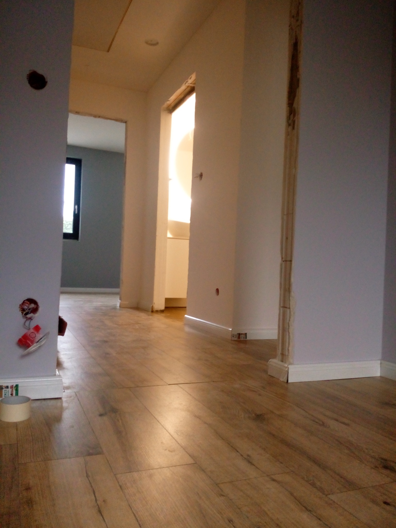 Fragment wnętrza w trakcie prac wykończeniowych, widoczne drewniane panele podłogowe, ściany w kolorze lila z widocznymi puszkami elektrycznymi i niezamaskowanymi futrynami drzwiowymi, w tle jasne...