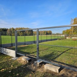 DS PŁOT - TRANS SYLWIA MARSZAŁKOWSKA - Nowoczesne, grafitowe ogrodzenie panelowe z bramą dwuskrzydłową, osadzone na betonowej podmurówce, widoczne na tle zielonego trawnika i drzew w jesiennej scenerii.